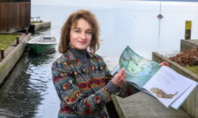 Gabriela Costea in front of Lake Müggelsee, holding the children's book in her hands. 