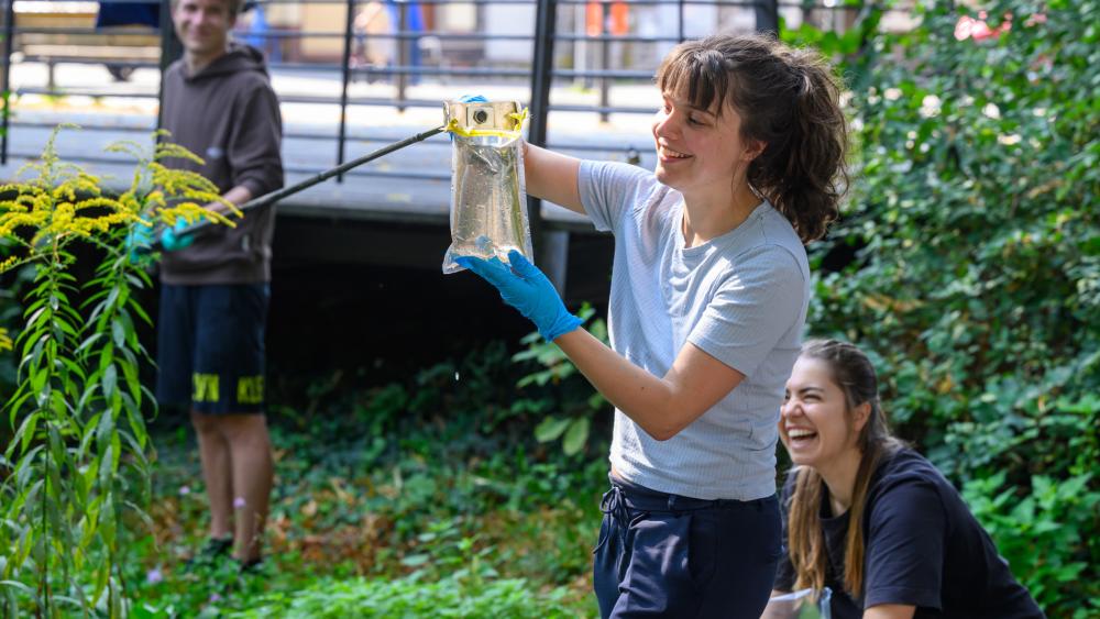 An IGB PhD student is taking a water sample from a pond in Berlin. She is being assisted by two colleagues.