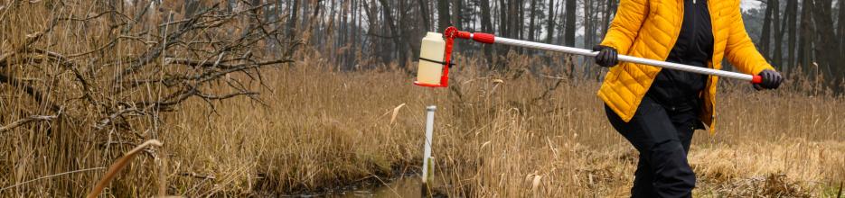 Dekoratives Bild: Eine Person nimmt eine Wasserprobe an einem Graben.